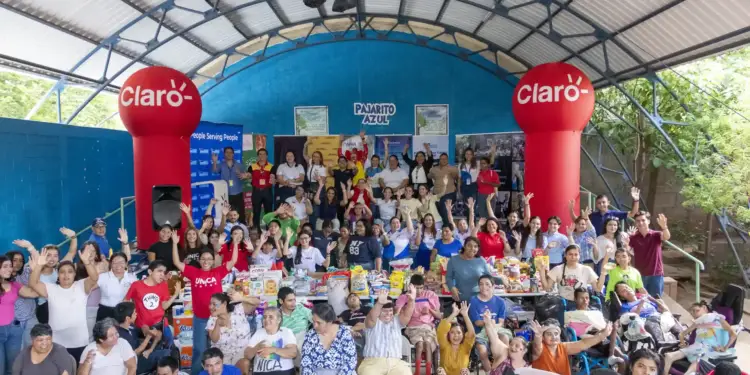 Gran grupo de personas, incluyendo usuarios de sillas de ruedas, sonríen y saludan en un evento de donación con marcas Claro y DHL.