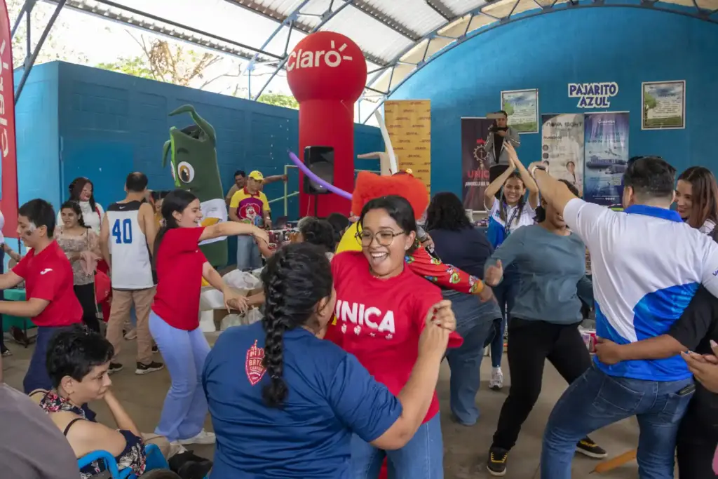 Grupo diverso de personas bailando y celebrando en un evento comunitario. Se aprecian logos de Claro, DHL, UNICA y Pajarito Azul, indicando patrocinio empresarial.