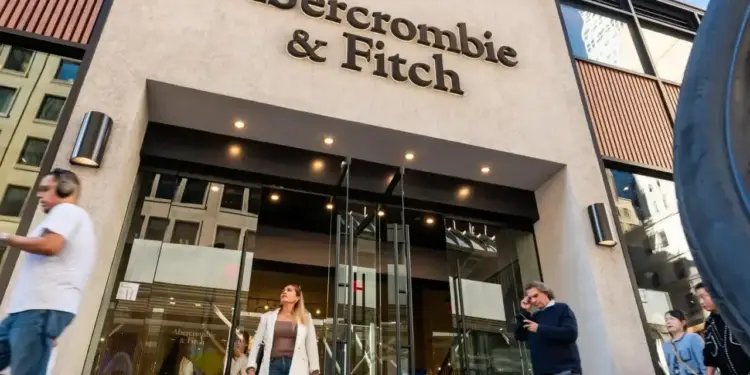 Fachada de la tienda Abercrombie & Fitch con el logotipo en relieve y personas caminando frente a la entrada.