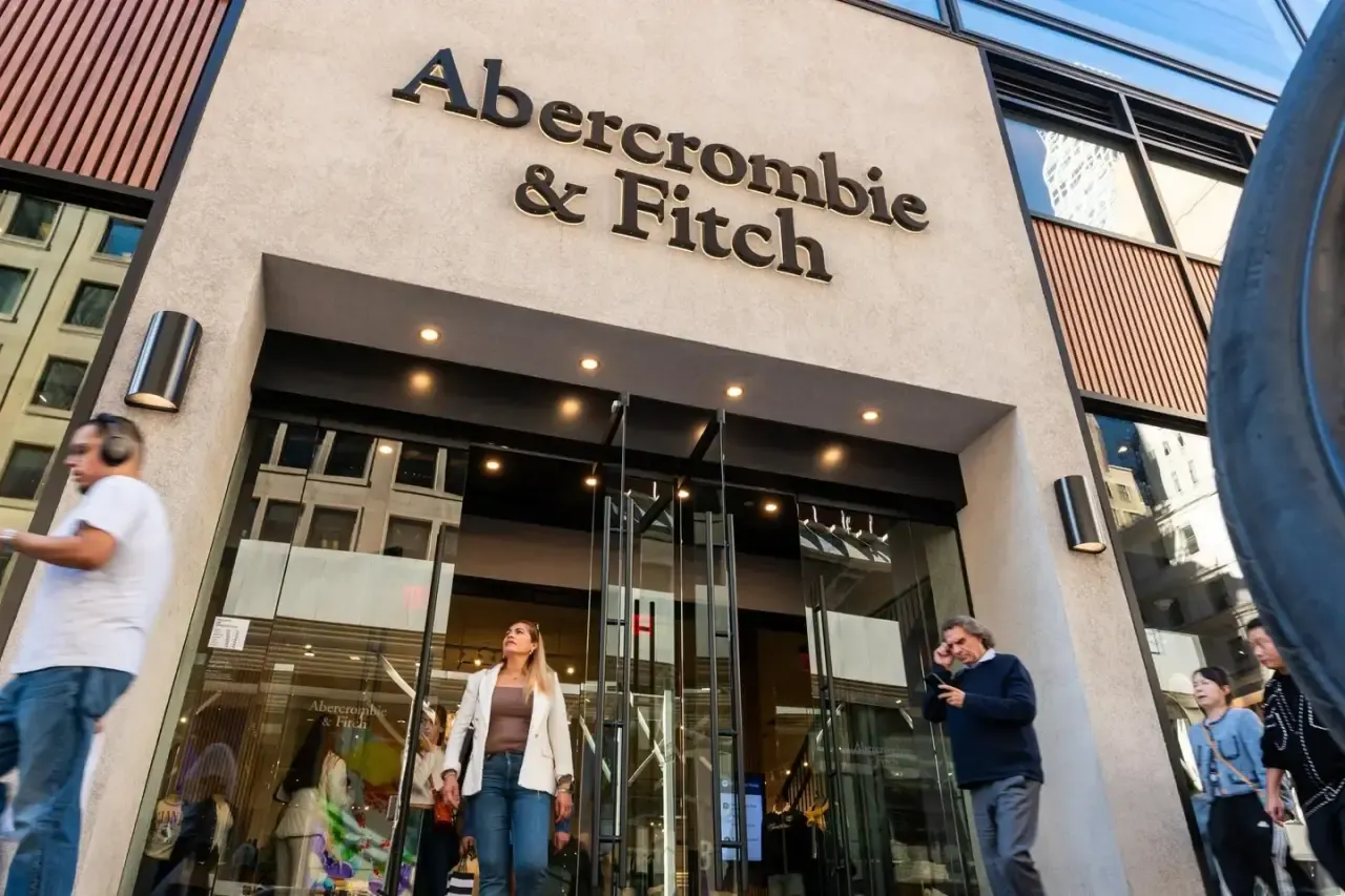 Fachada de la tienda Abercrombie & Fitch con el logotipo en relieve y personas caminando frente a la entrada.