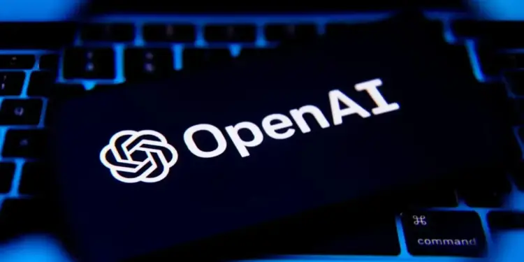 Logotipo de OpenAI iluminado en color blanco sobre la pantalla de un dispositivo colocado encima de un teclado iluminado en azul.