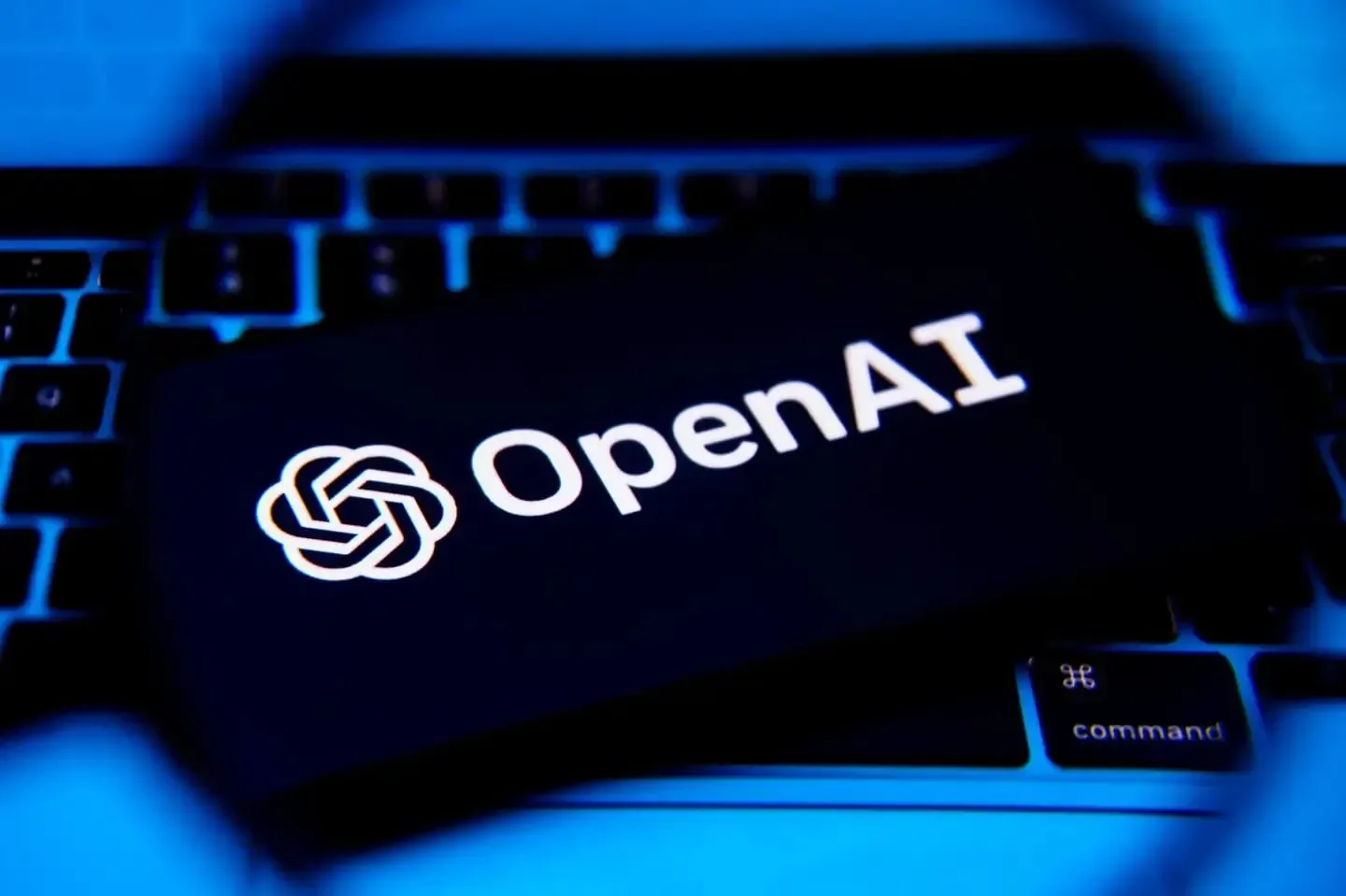 Logotipo de OpenAI iluminado en color blanco sobre la pantalla de un dispositivo colocado encima de un teclado iluminado en azul.