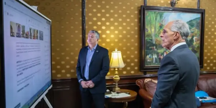 Dos hombres de traje observando una pantalla digital grande durante una reunión de negocios en una oficina elegante.