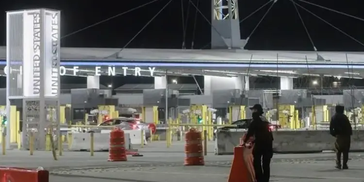 Vista nocturna de un puerto de entrada oficial con letreros iluminados y personal de seguridad vigilando la zona.