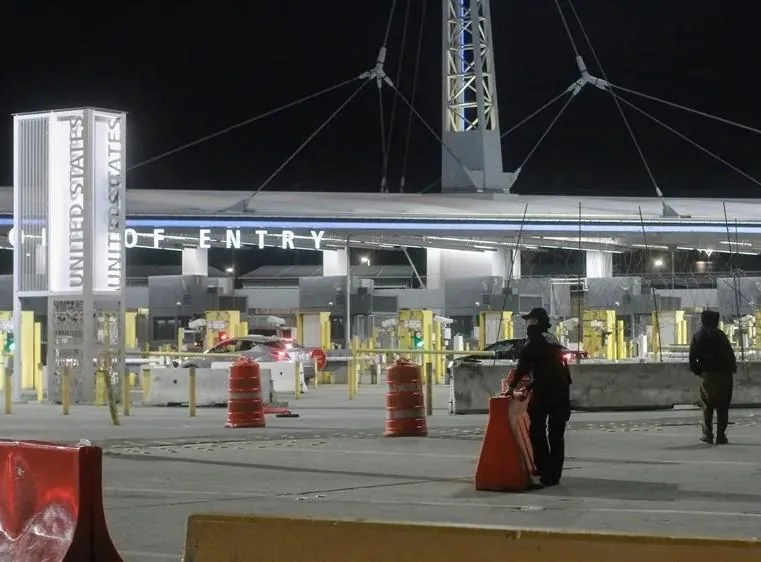 Vista nocturna de un puerto de entrada oficial con letreros iluminados y personal de seguridad vigilando la zona.