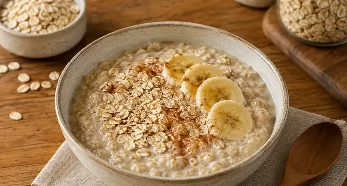 Tazón de avena cremosa con rodajas de plátano y canela sobre una mesa de madera.