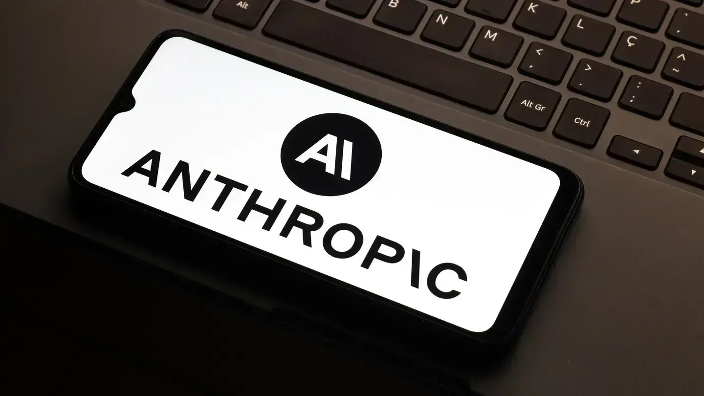 Teléfono inteligente mostrando el logotipo y nombre de Anthropic en su pantalla, colocado sobre una laptop.