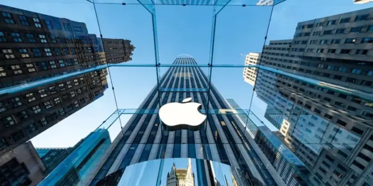 Vista en contrapicado de un cubo de cristal transparente con un logotipo corporativo en el centro, rodeado de rascacielos y cielo azul.
