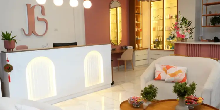 Recepción blanca iluminada con mostrador, sofás en el área de espera y estantes con productos en un negocio moderno.