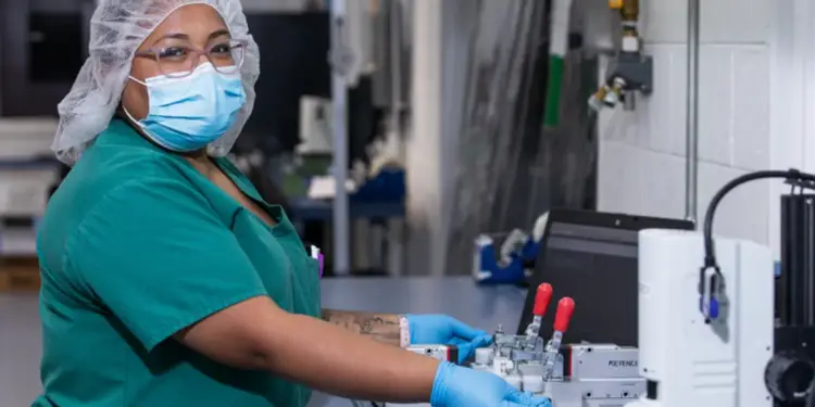 Trabajadora industrial con cofia, mascarilla y guantes utilizando maquinaria en una planta de producción.