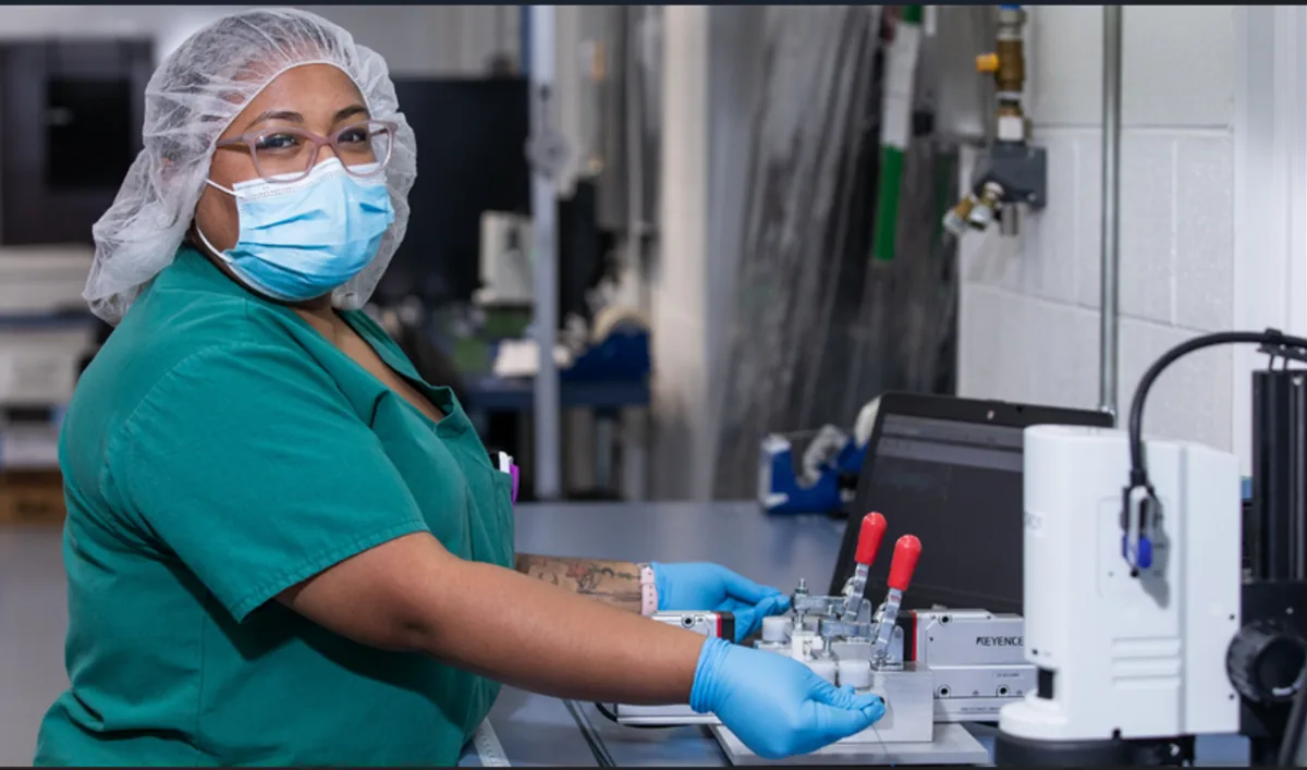 Trabajadora industrial con cofia, mascarilla y guantes utilizando maquinaria en una planta de producción.