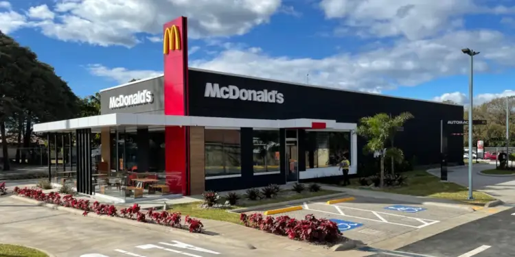 Vista exterior de un restaurante McDonald's con fachada moderna, letrero rojo y amarillo, y estacionamiento.
