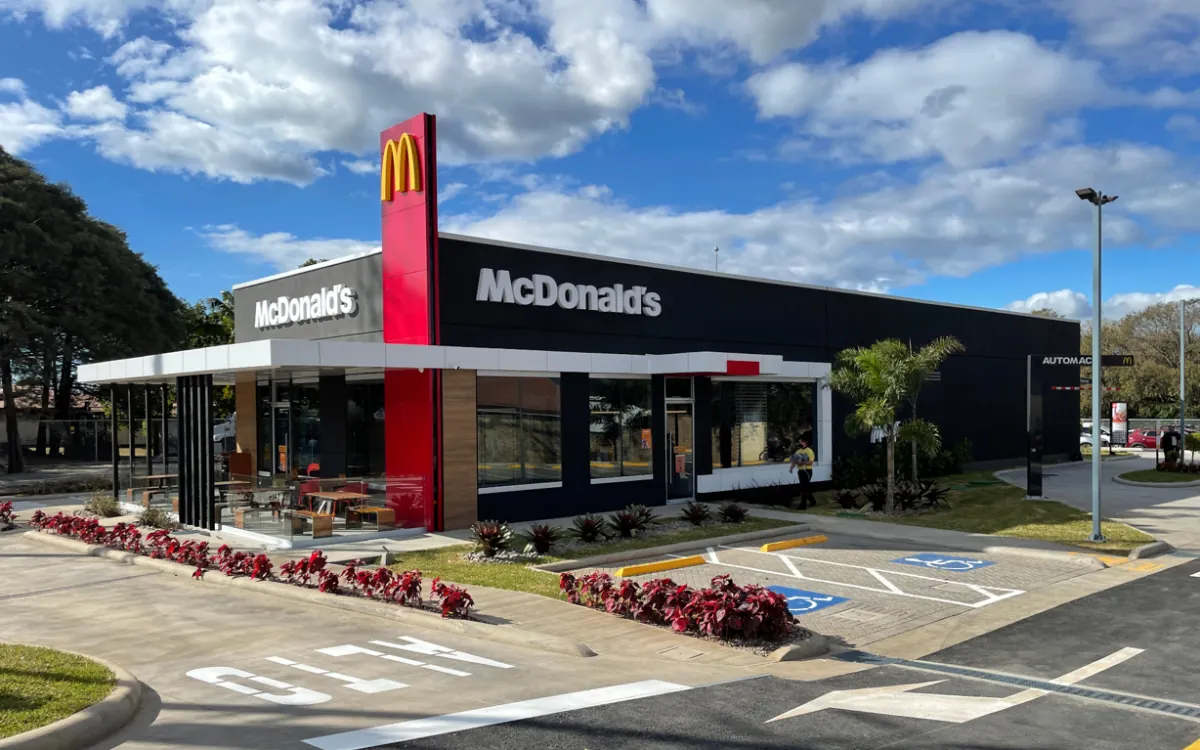 Vista exterior de un restaurante McDonald's con fachada moderna, letrero rojo y amarillo, y estacionamiento.