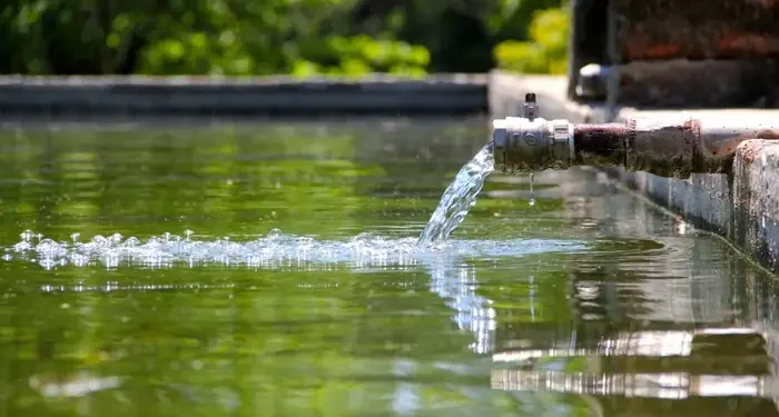 Agua fluyendo desde una tubería metálica hacia un estanque exterior, representando el suministro y uso de recursos hídricos.