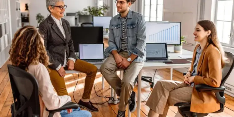 Cuatro profesionales reunidos en una oficina moderna discutiendo estrategias de negocio frente a computadoras.