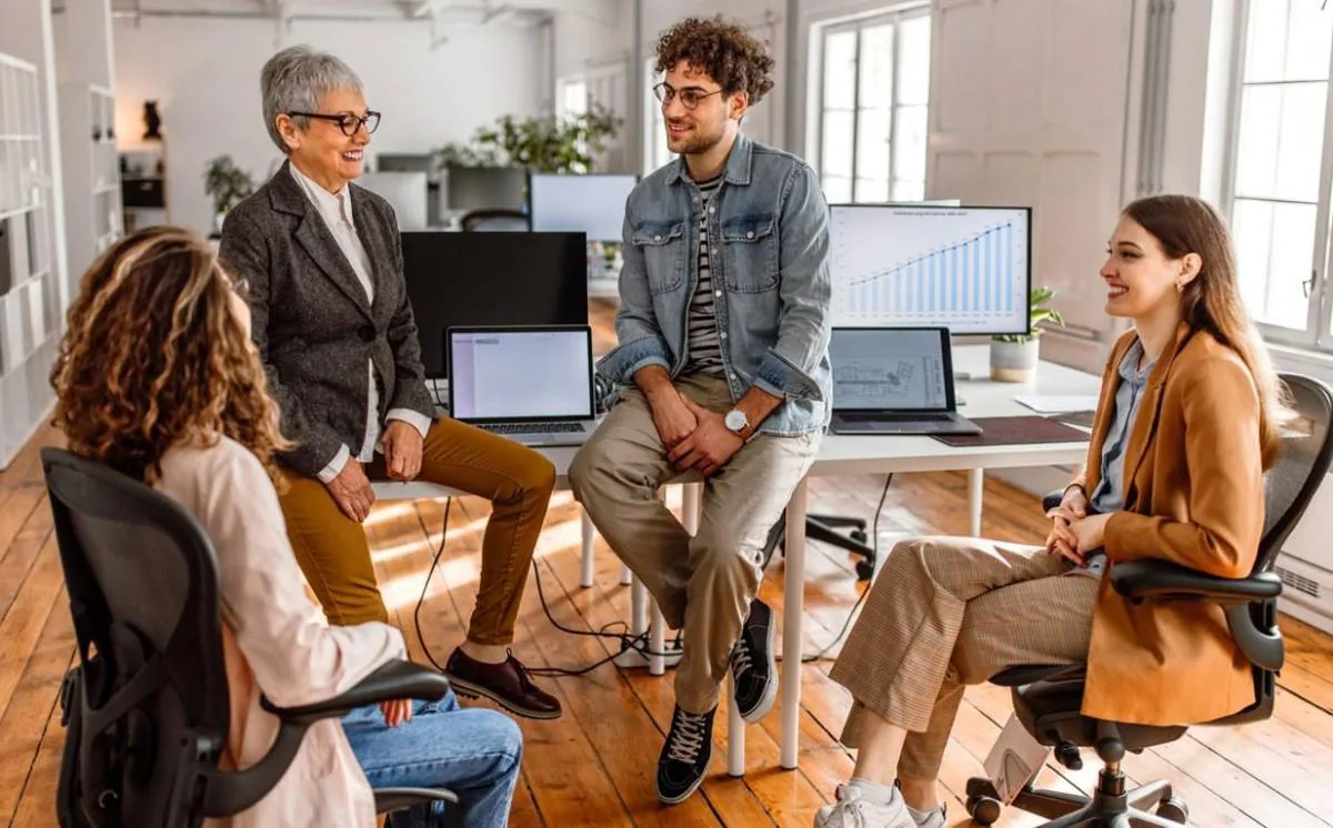 Cuatro profesionales reunidos en una oficina moderna discutiendo estrategias de negocio frente a computadoras.