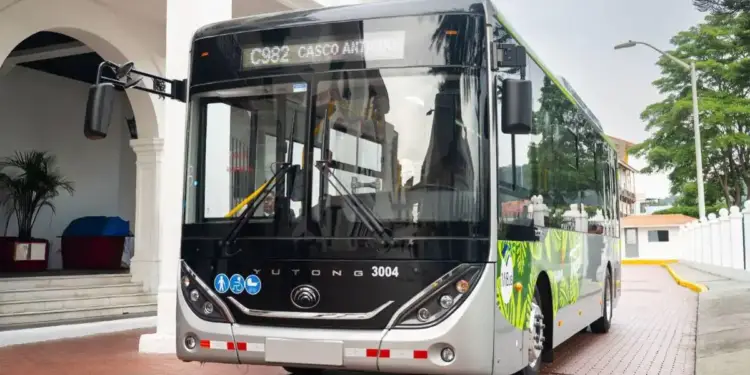 Autobús de transporte público moderno detenido en una calle adoquinada frente a un edificio con columnas blancas.