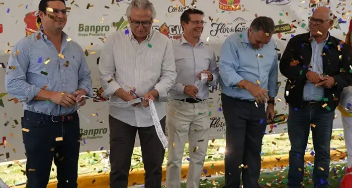 Cinco hombres de negocios cortando una cinta durante una ceremonia de inauguración con confeti cayendo