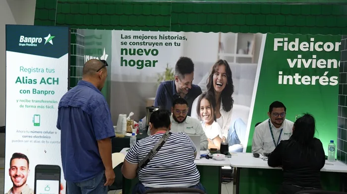 Stand de Banpro Grupo Promerica con banners sobre Alias ACH y financiamiento de hogar. Personal atiende a clientes en un evento.