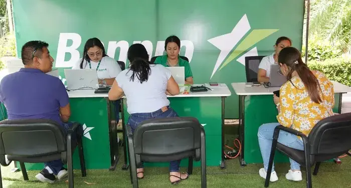 Personas sentadas en escritorios atendiendo a clientes en un espacio corporativo con fondo verde y el logo de una estrella.