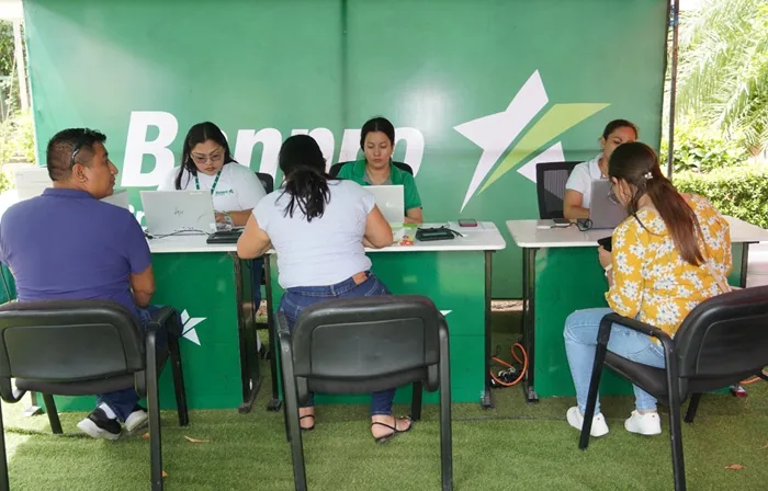Personas sentadas en escritorios atendiendo a clientes en un espacio corporativo con fondo verde y el logo de una estrella.