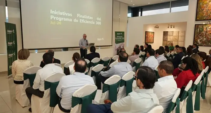 Un ponente habla frente a una pantalla grande con texto corporativo ante un público sentado en sillas.