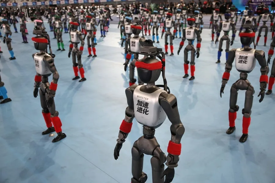 Gran grupo de robots humanoides de pie alineados en un suelo azul en una exhibición de tecnología.