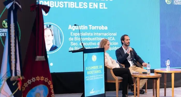 Un hombre con micrófono y una mujer sentados en un panel frente a una pantalla sobre biocombustibles en una conferencia.