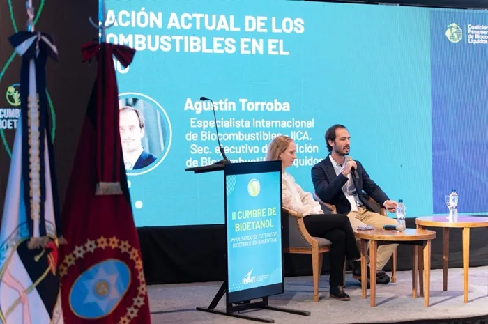 Un hombre con micrófono y una mujer sentados en un panel frente a una pantalla sobre biocombustibles en una conferencia.