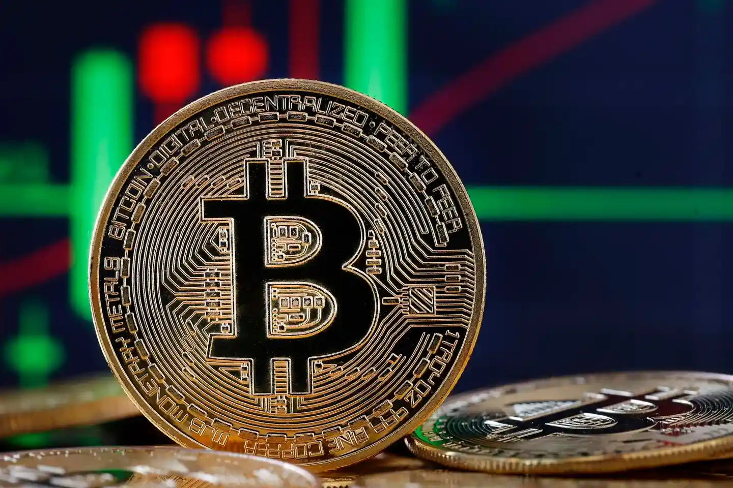 Primer plano de una moneda de Bitcoin dorada con el símbolo 'B' en el centro, sobre un fondo de gráficos financieros con barras verdes y rojas.