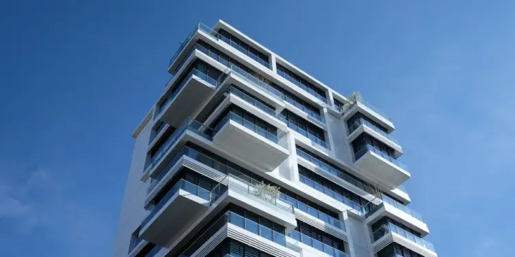 Edificio moderno de múltiples pisos con fachada blanca y balcones de cristal bajo un cielo azul claro. Representa inversión inmobiliaria y desarrollo urbano.
