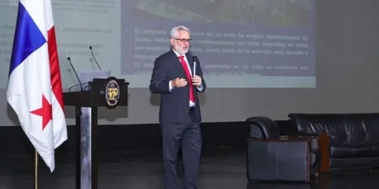 Ponente en conferencia de negocios, con bandera panameña y pantalla mostrando datos de un proyecto, en un auditorio.