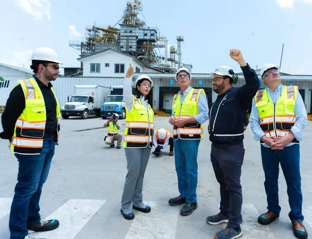 Grupo de profesionales con cascos y chalecos de seguridad inspeccionando una planta industrial con camiones de carga.