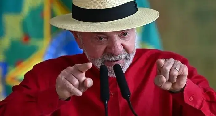 Hombre maduro con sombrero de ala ancha y camisa roja apuntando con ambos dedos índices hacia el frente.