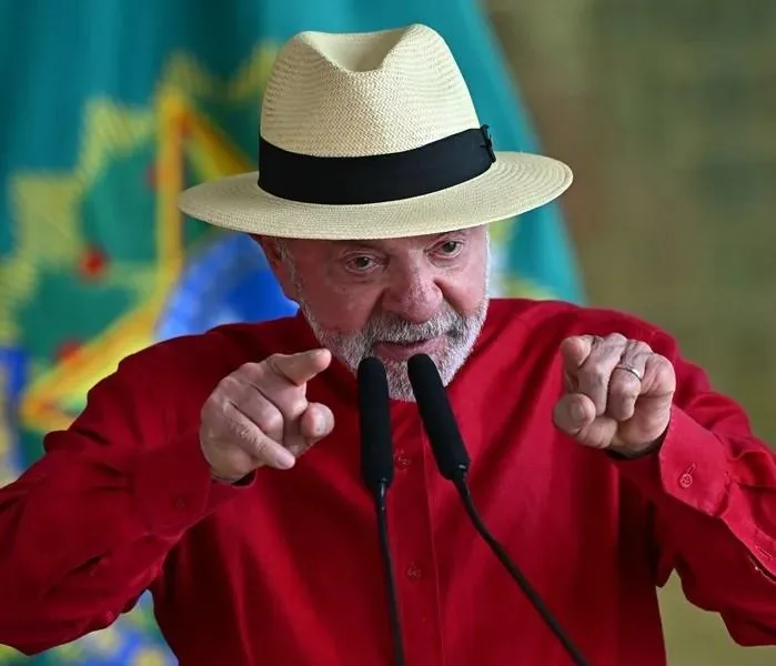 Hombre maduro con sombrero de ala ancha y camisa roja apuntando con ambos dedos índices hacia el frente.