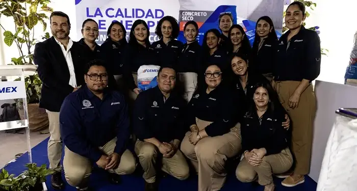 Grupo de profesionales sonrientes posando juntos en un evento corporativo frente a un cartel publicitario.