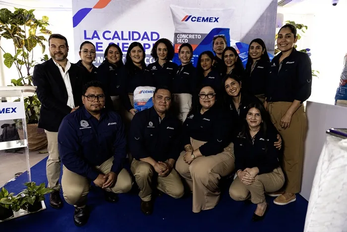 Grupo de profesionales sonrientes posando juntos en un evento corporativo frente a un cartel publicitario.