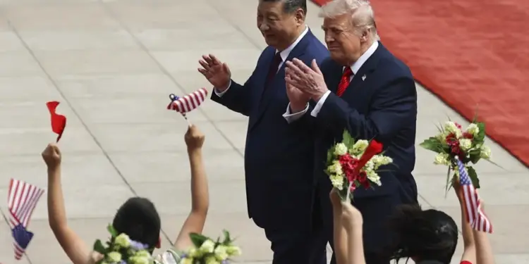 Dos líderes políticos, uno con traje azul y corbata roja, saludan a una multitud de niños que ondean banderas de EE. UU. y flores.