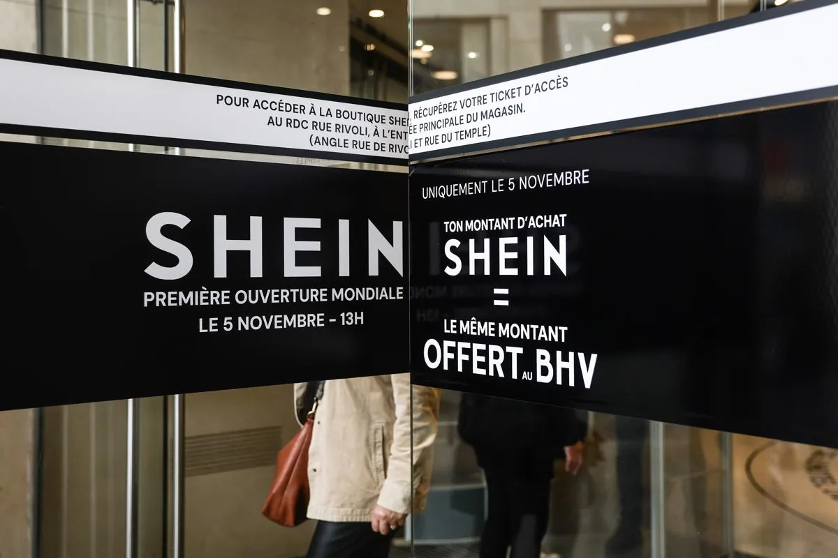 Carteles negros con letras blancas anuncian la apertura mundial de la tienda Shein el 5 de noviembre, con una promoción de compra igualada por BHV, en la entrada de un establecimiento.
