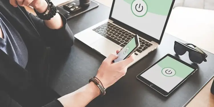 Persona trabajando con una laptop, smartphone y tablet con el símbolo de encendido en la pantalla