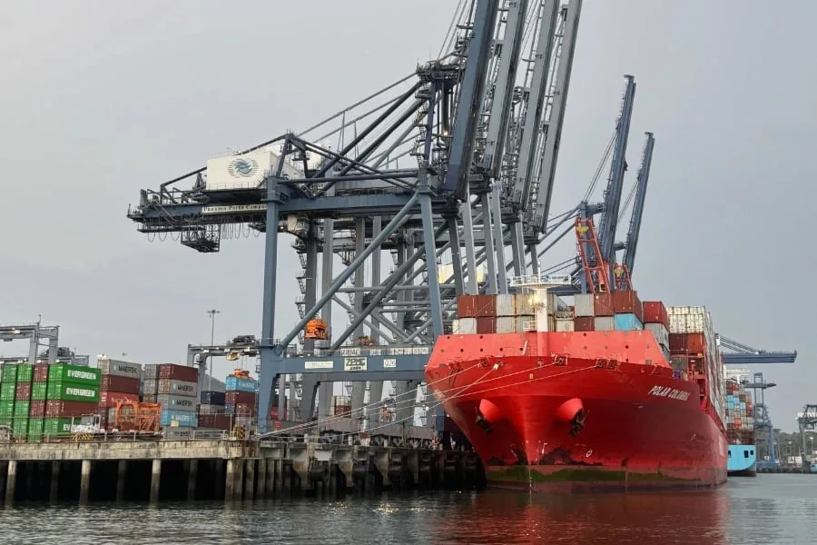 Gran barco de carga rojo, el 'Polar Colombia', atracado en un puerto con múltiples grúas portuarias y pilas de contenedores de envío.