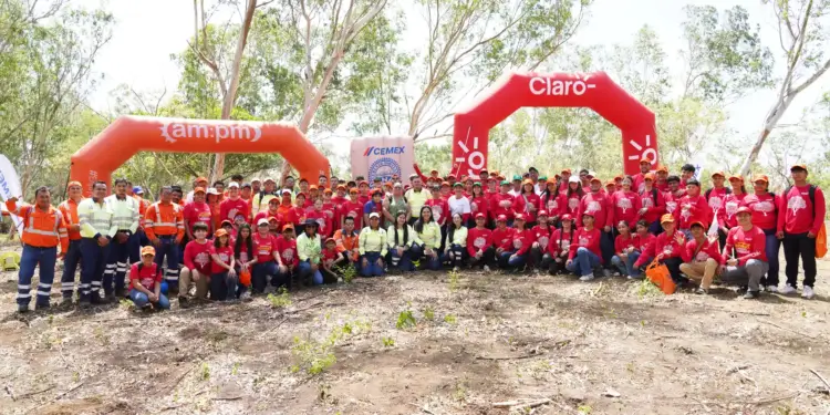 Amplio grupo de personas sonrientes vestidas con camisas rojas reunidas en un bosque junto a arcos inflables corporativos.