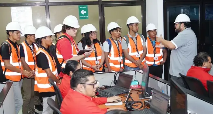 Grupo de personas con cascos y chalecos reflectantes recibiendo capacitación de un instructor en una oficina.