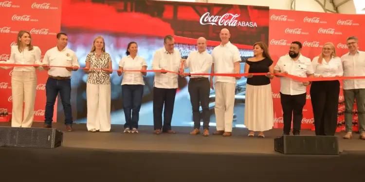 Grupo de diez personas cortando una cinta roja en un evento corporativo frente a un fondo rojo con logotipos.