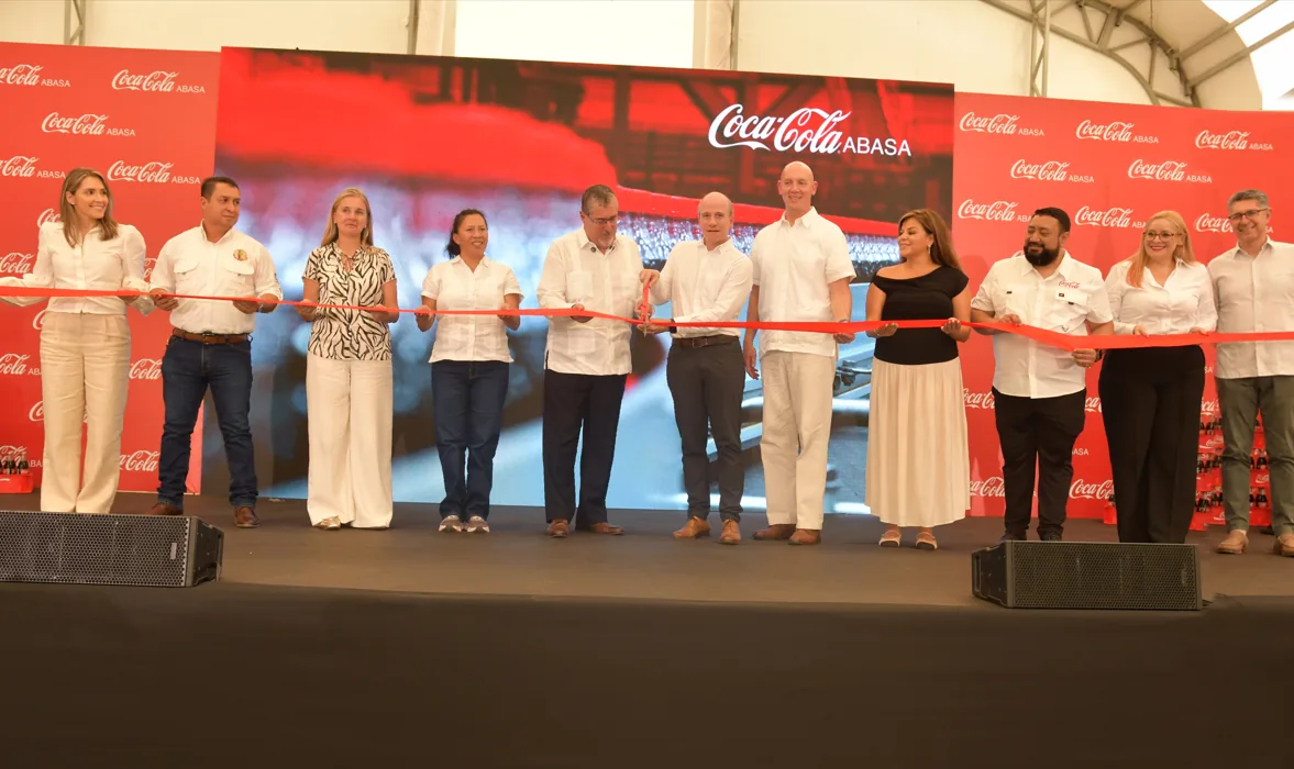 Grupo de diez personas cortando una cinta roja en un evento corporativo frente a un fondo rojo con logotipos.