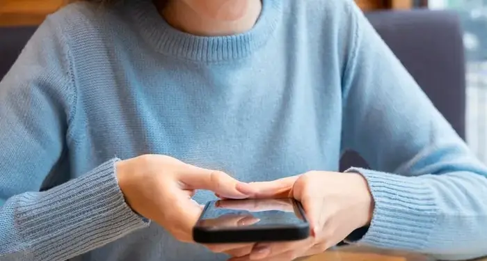 Mujer joven sonriente escaneando un código QR en la mesa con su teléfono móvil en un establecimiento