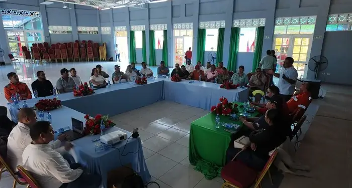 Grupo de personas sentadas alrededor de mesas dispuestas en U escuchando una presentación en un salón