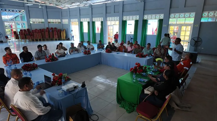Grupo de personas sentadas alrededor de mesas dispuestas en U escuchando una presentación en un salón