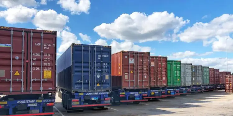 Fila de camiones estacionados transportando contenedores marítimos de colores bajo un cielo nublado