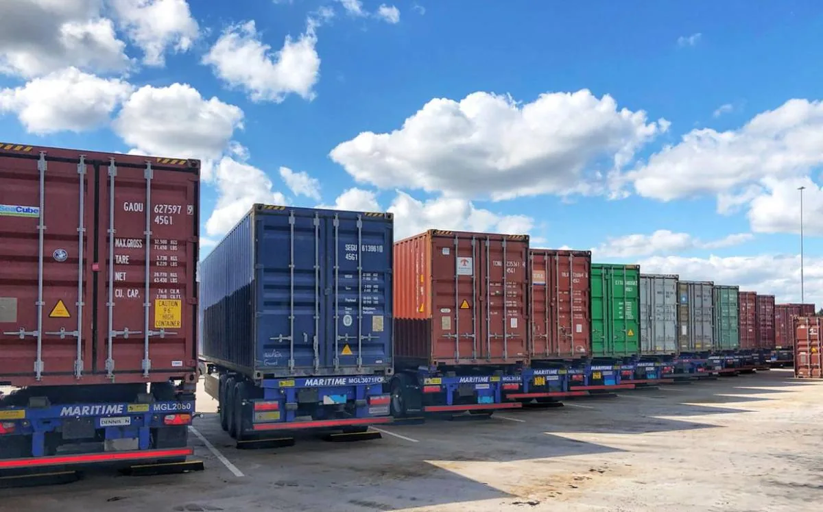 Fila de camiones estacionados transportando contenedores marítimos de colores bajo un cielo nublado
